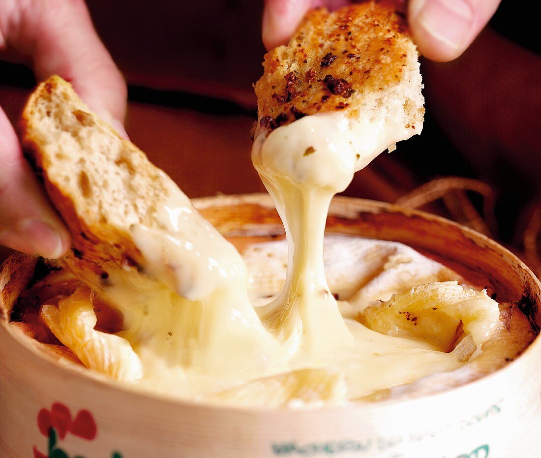 Hands dipping pieces of bread in melted Vacherin cheese