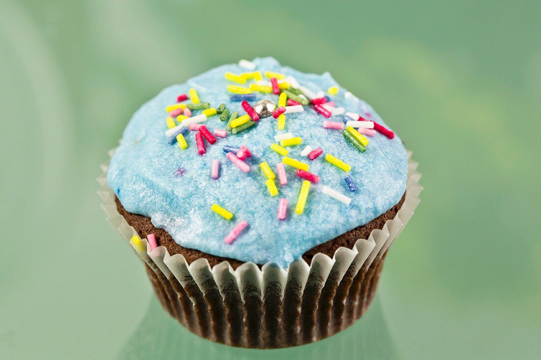 A chocolate cupcake decorated with blue buttercream icing and sugar strands