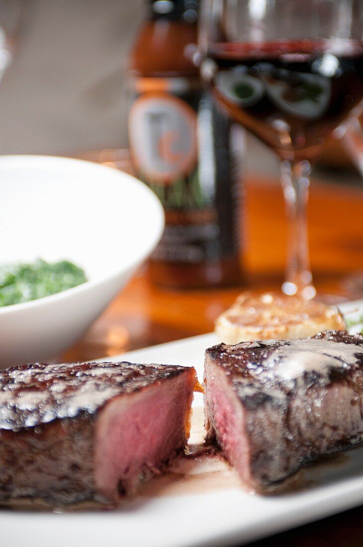 Halbiertes Steak auf einem Teller, Wein im Hintergrund