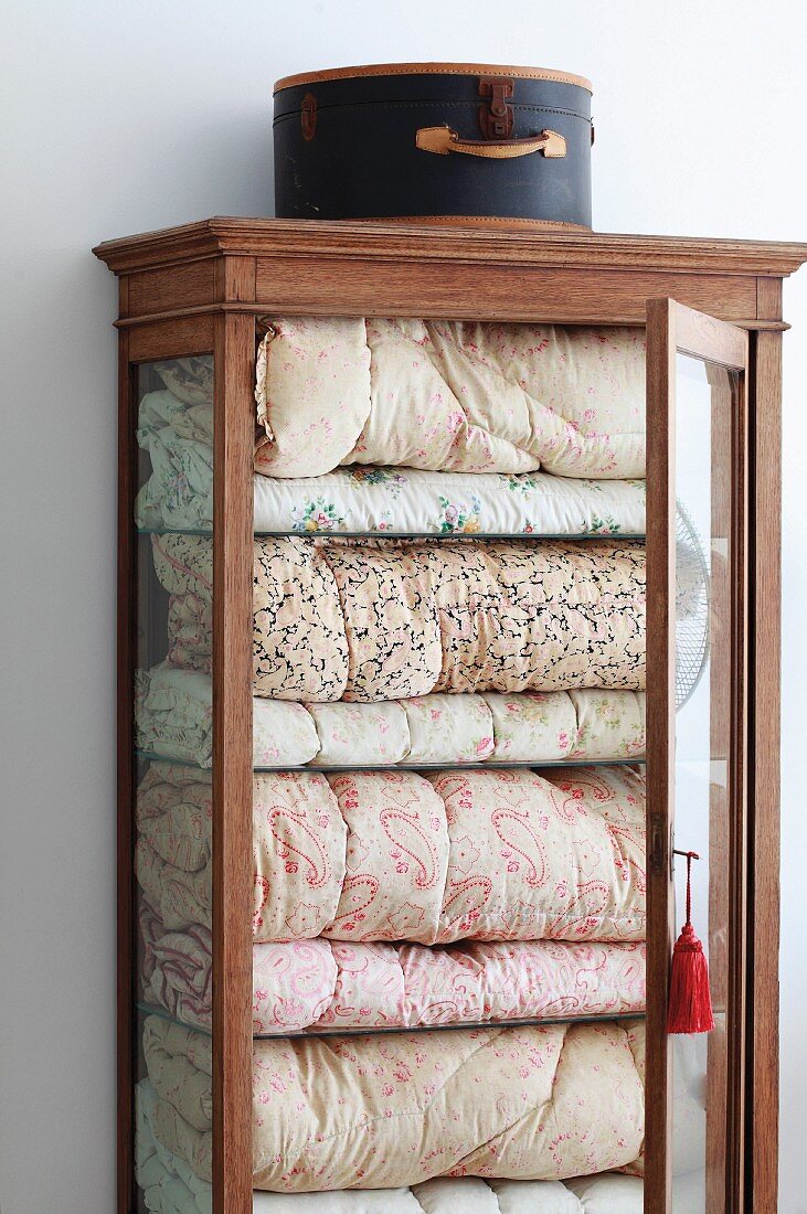 Vintage hatbox on display case with open door and view of stacked bedspreads