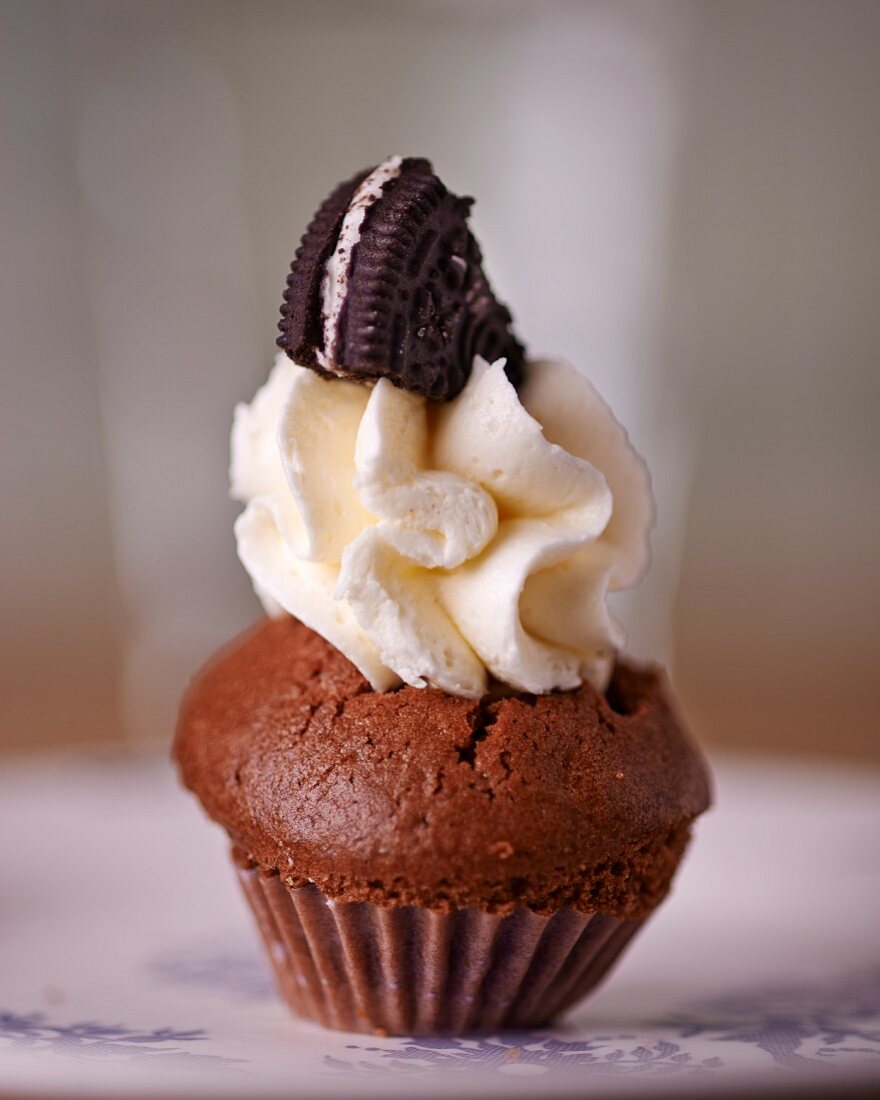 A chocolate cupcake topped with cream and a chocolate biscuit