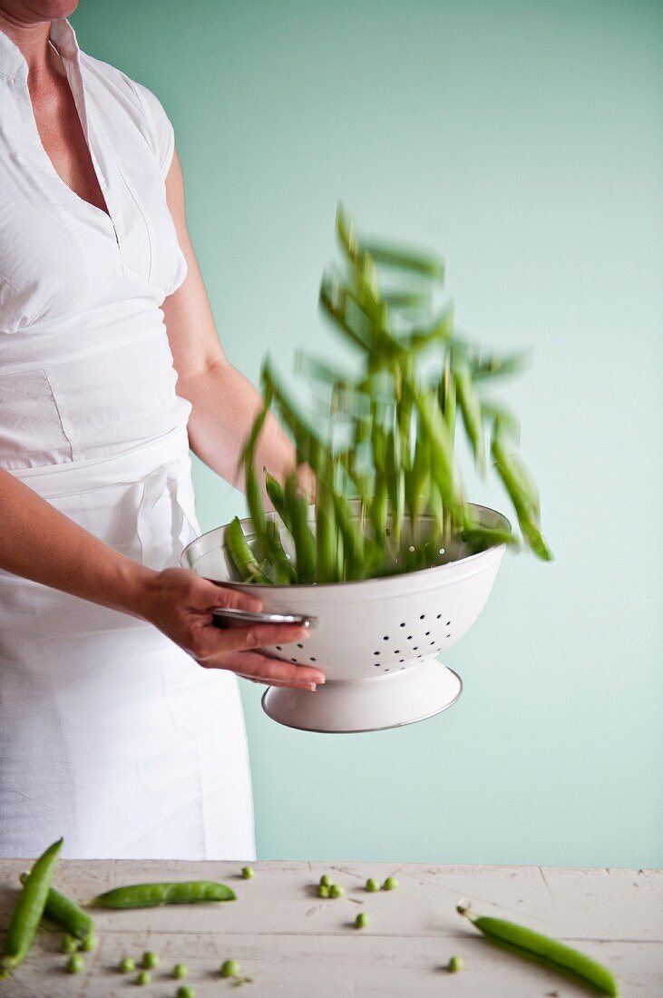 A cook tossing pea pods in a colander