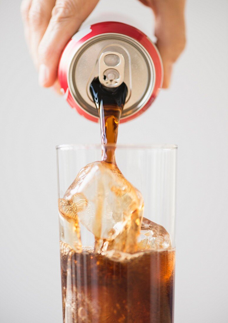 Cola in ein Glas mit Eiswürfeln gießen
