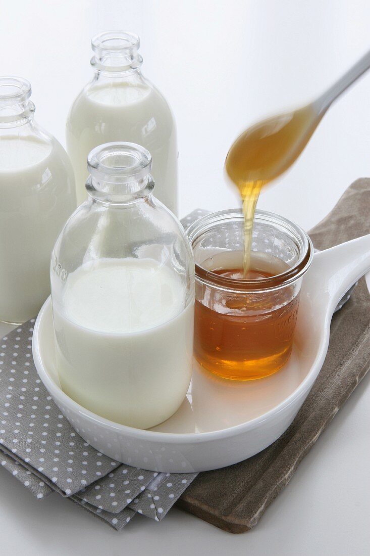 A bottle of milk and a glass of honey with honey dripping into it