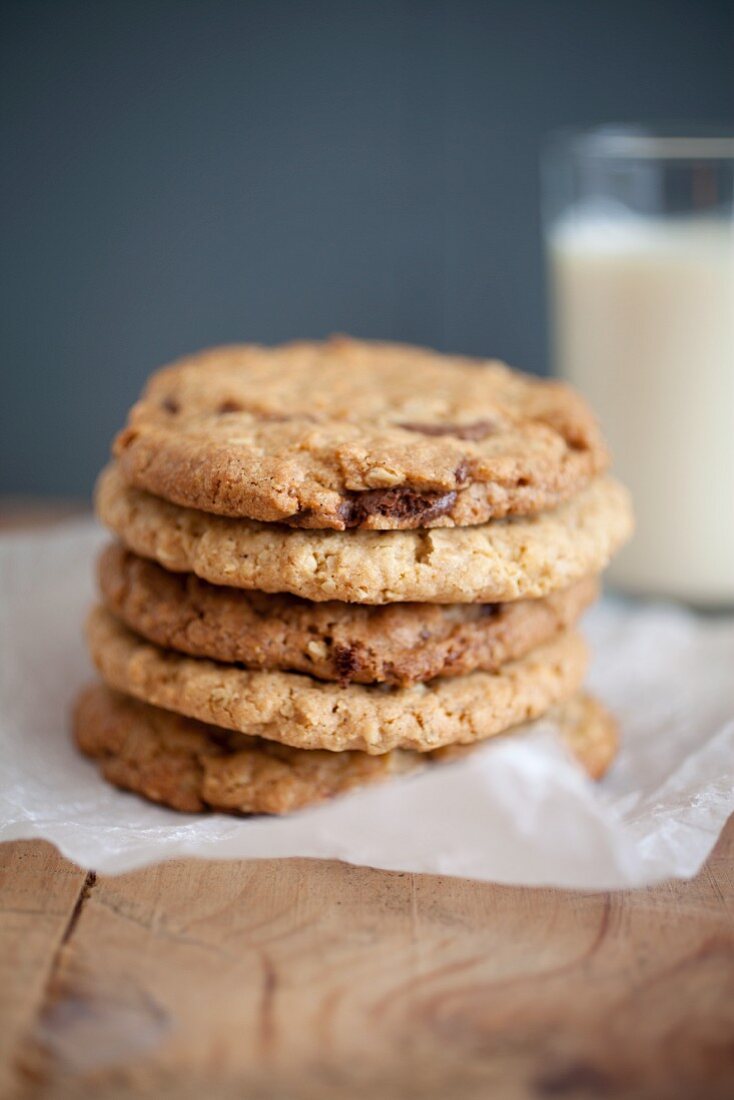 Chocolatechip Cookies mit Erdnussbutter und Haferflocken auf Backpapier vor einem Milchglas