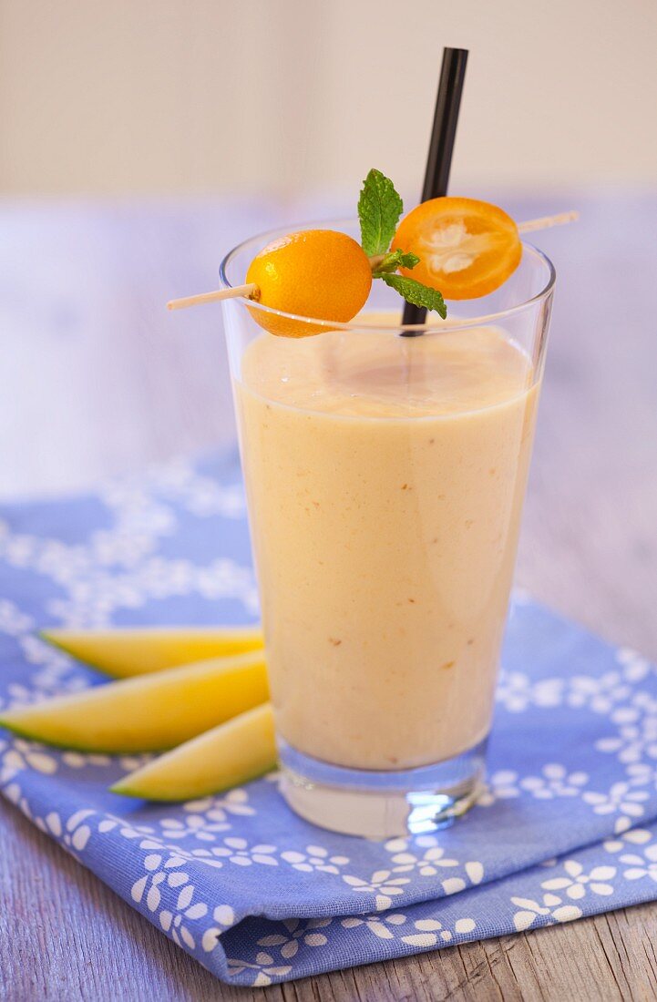 Exotischer Smoothie mit Mango und Kumquats auf blauer Serviette und Holzplatte