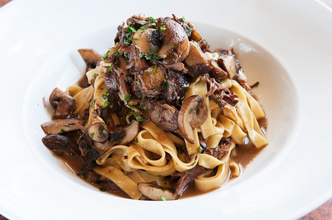 Tagliatelle with Wild Mushrooms, Fresh Herbs, Braised Short Ribs and Brown Sauce in a White Bowl