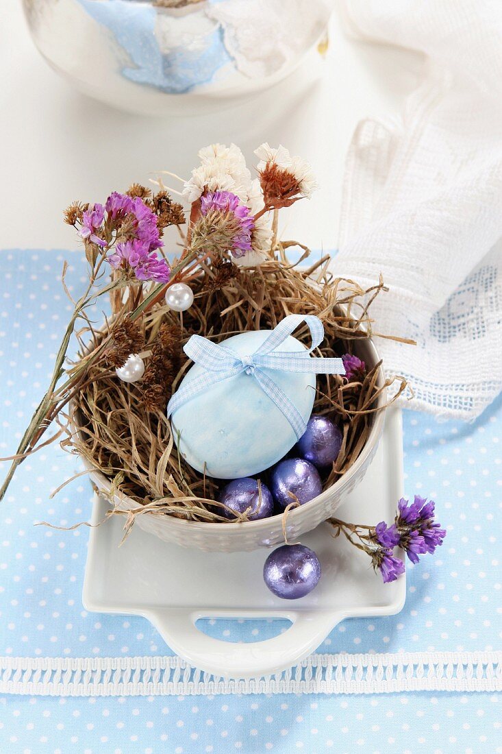 Ei mit Schleife, Trockenblumen und Schokoeier im Osternest aus Moos und Gras