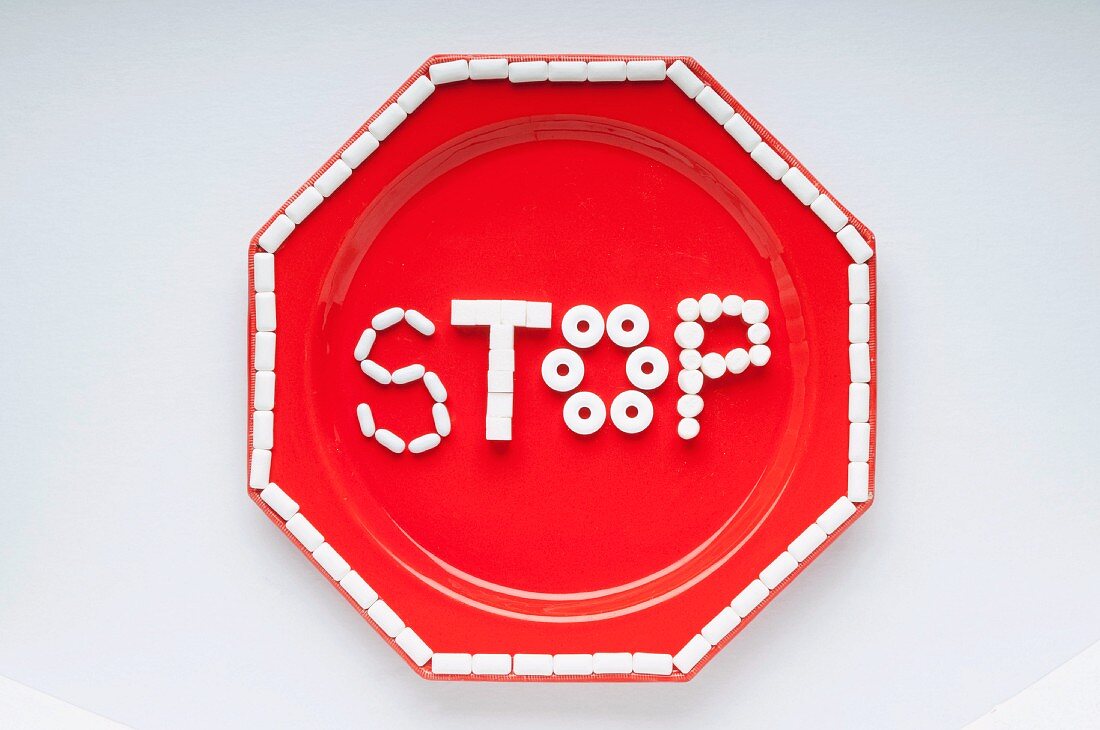 The Word Stop Spelled Out with White Candies on a Red Plate; From Above; White Background