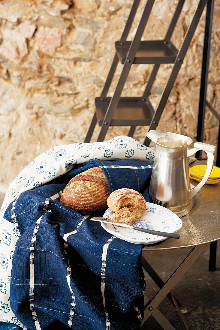Blue and white patterned tablecloths, silver pitcher and Dutch plate of bread on metal table