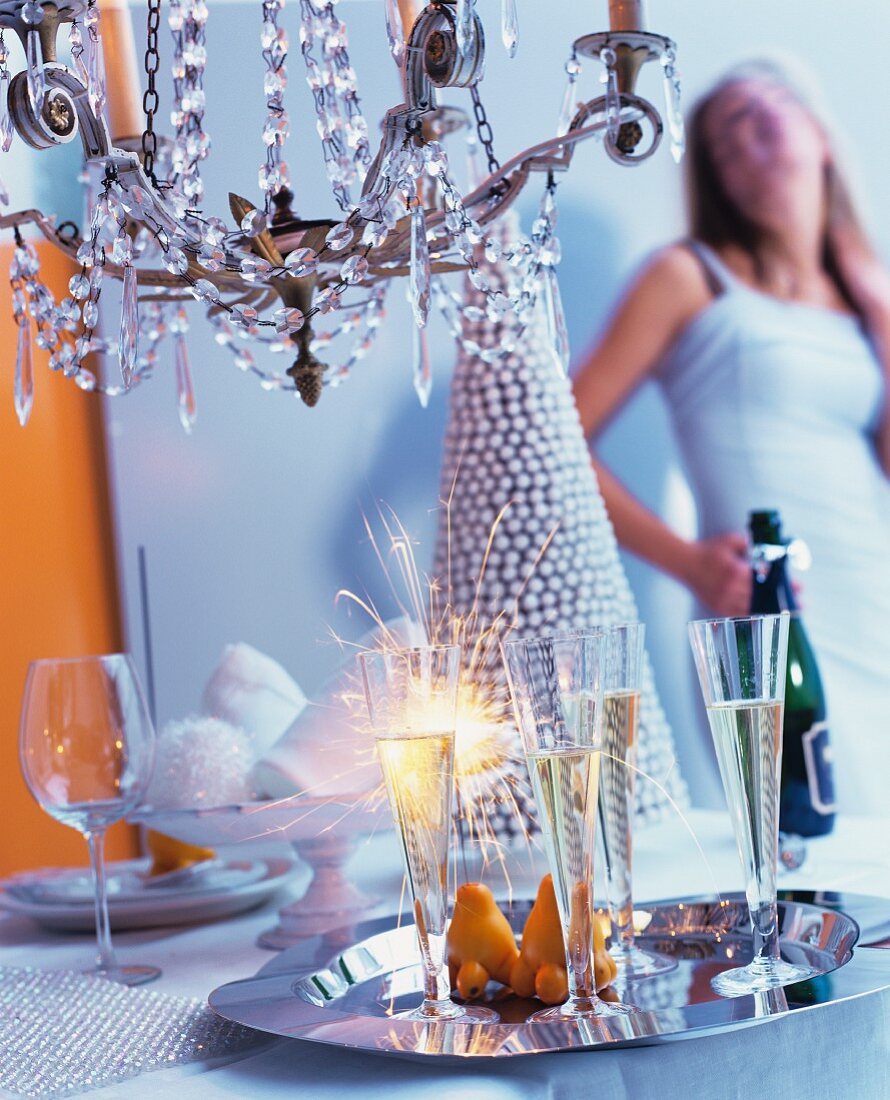 Sektflöten & Wunderkerzen auf Tablett unter Kronleuchter, im Hintergrund Partygäste