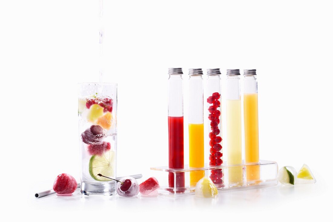 A glass of water with fruits in, and frozen fruits and juices in glass tubes