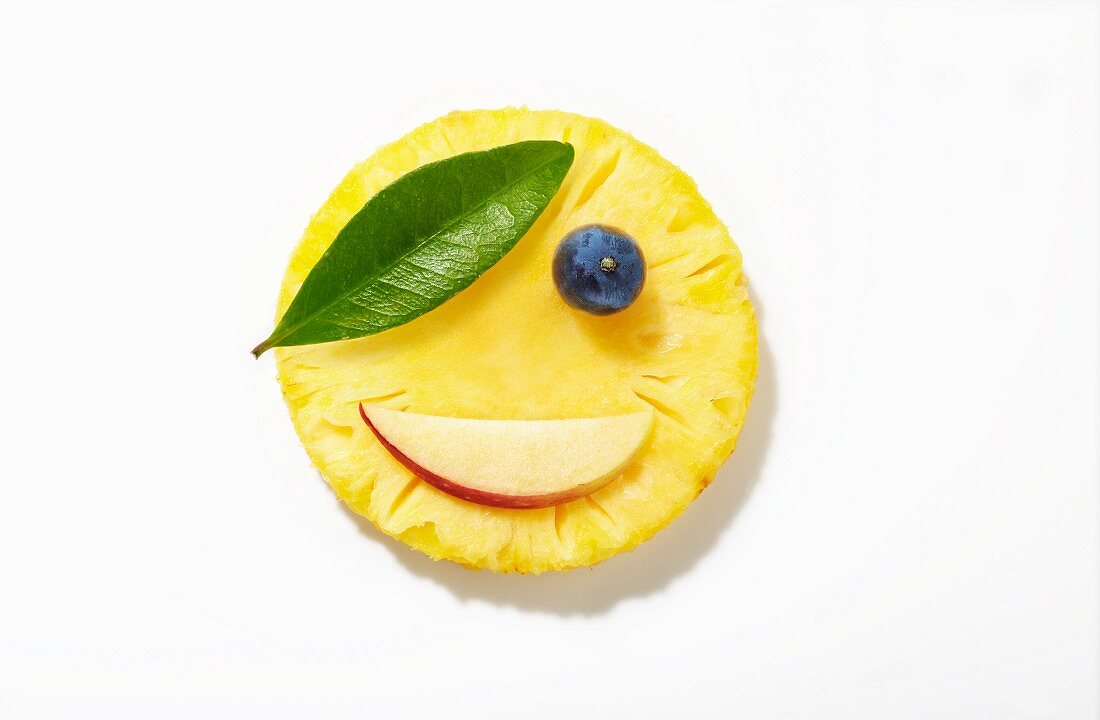 A pirate face made from pineapple, apple, a blueberry and a leaf