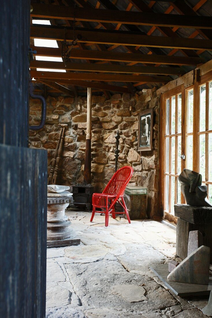 Red-painted wicker chair on stone flagged floor in interior of rustic Italian farmhouse