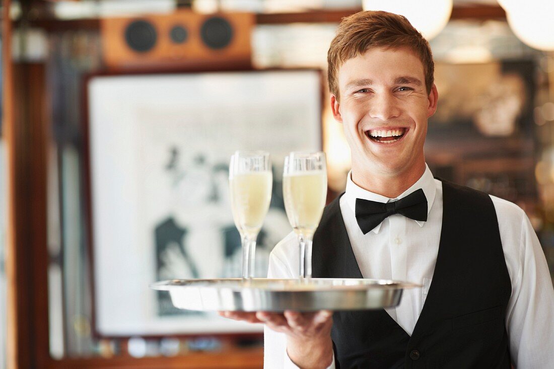 A waiter holding a tray with two glasses of sparkling wine in a restaurant