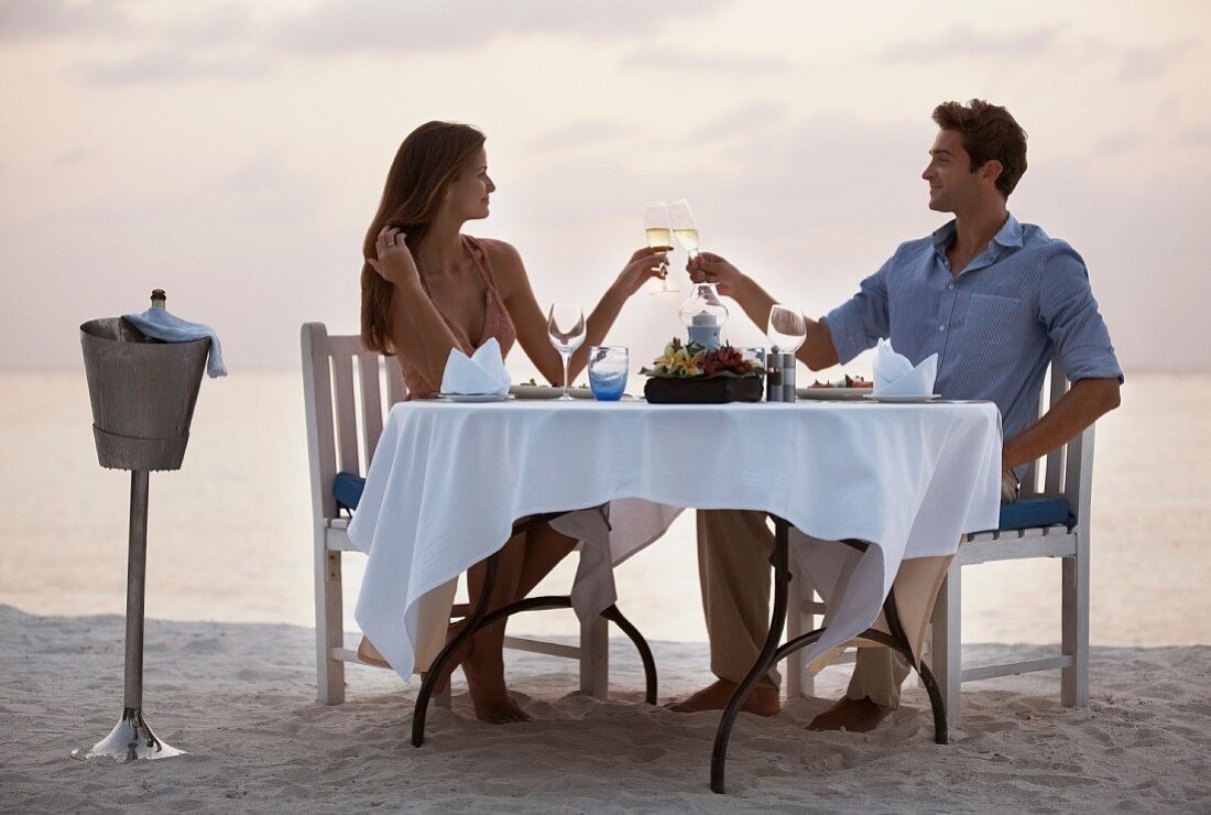 Paar stösst mit Sektgläsern an beim Dinner for Two am Sandstrand
