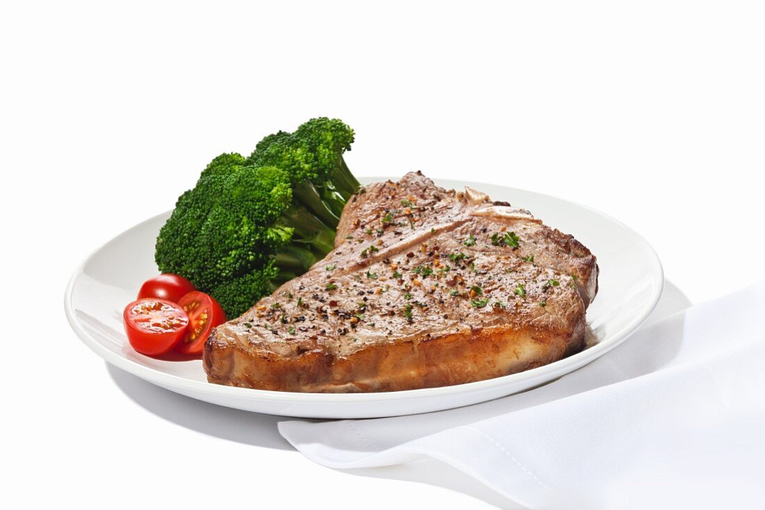 Seasoned T-Bone Steak with Cherry Tomatoes and Broccoli on a White Background
