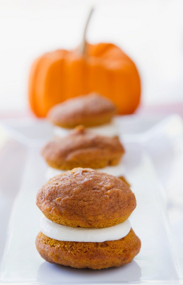 Three Mini Pumpkin Whoopie Pies on a White Platter with a Pumpkin in the Background