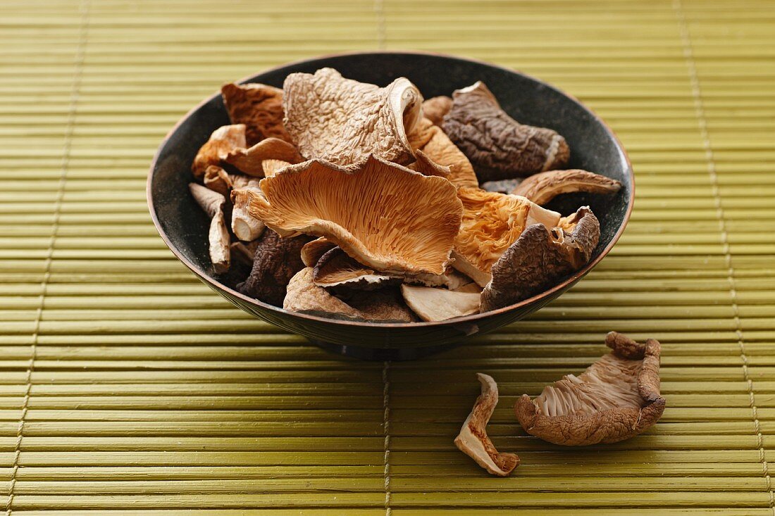 Dried oyster mushrooms in a bowl on a bamboo mat