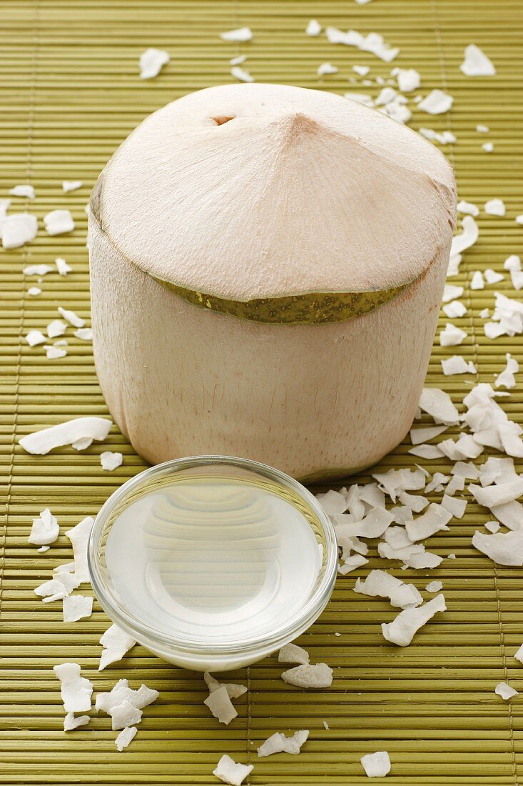 Geschälte Kokosnuss, Kokoswasser und Kokosraspeln auf Bambusmatte