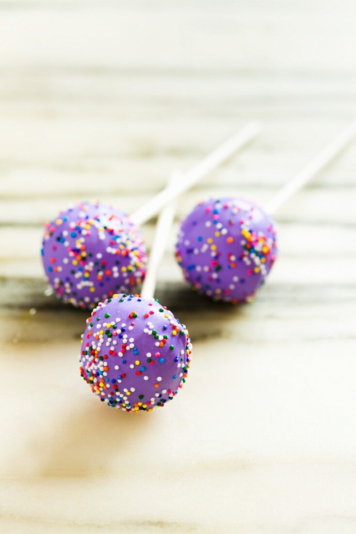 Three Purple Frosted Cake Pops with Rainbow Colored Sprinkles