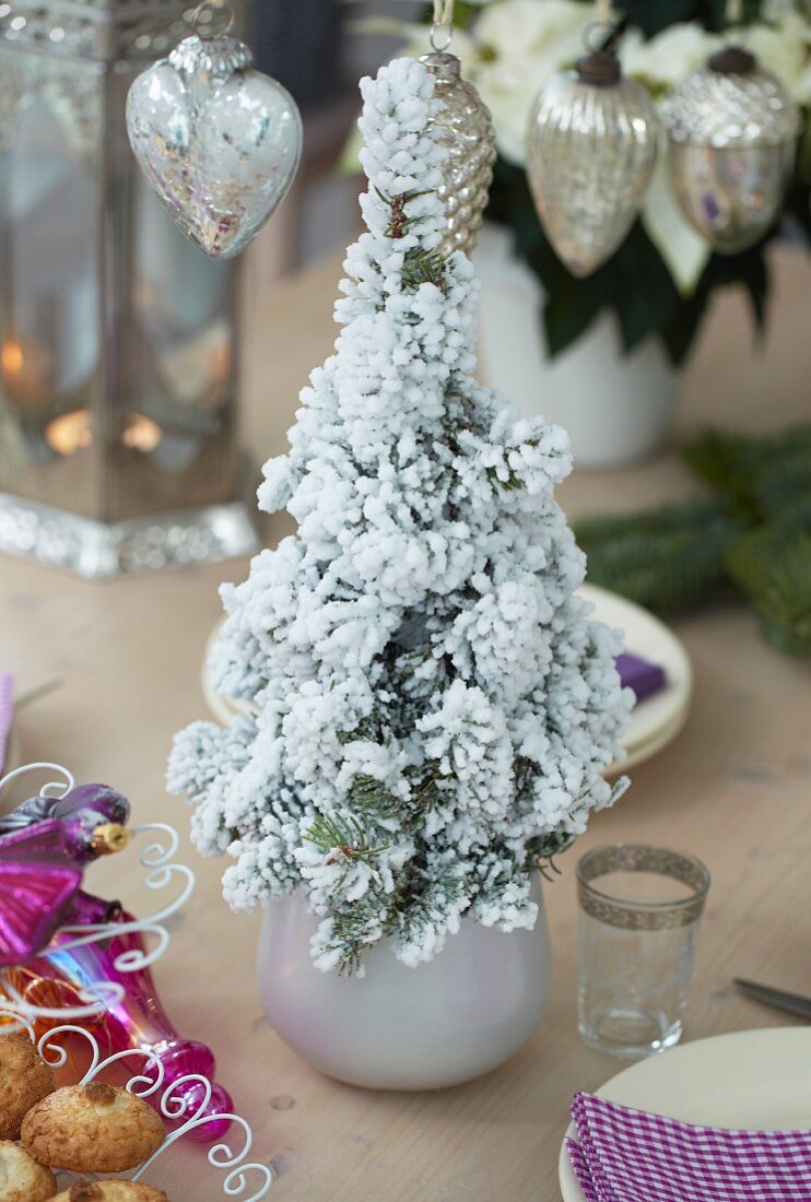 Mini-Christbaum mit Kunstschnee als Mittelpunkt auf gedecktem Tisch