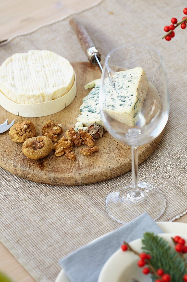 Soft cheese, blue cheese, a cheese knife, nuts and figs on a wooden platter