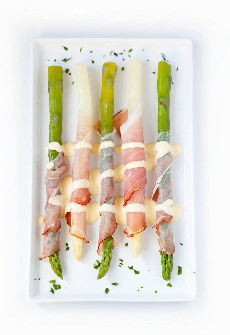 Asparagus wrapped in ham with Hollandaise sauce, on a tray; no background