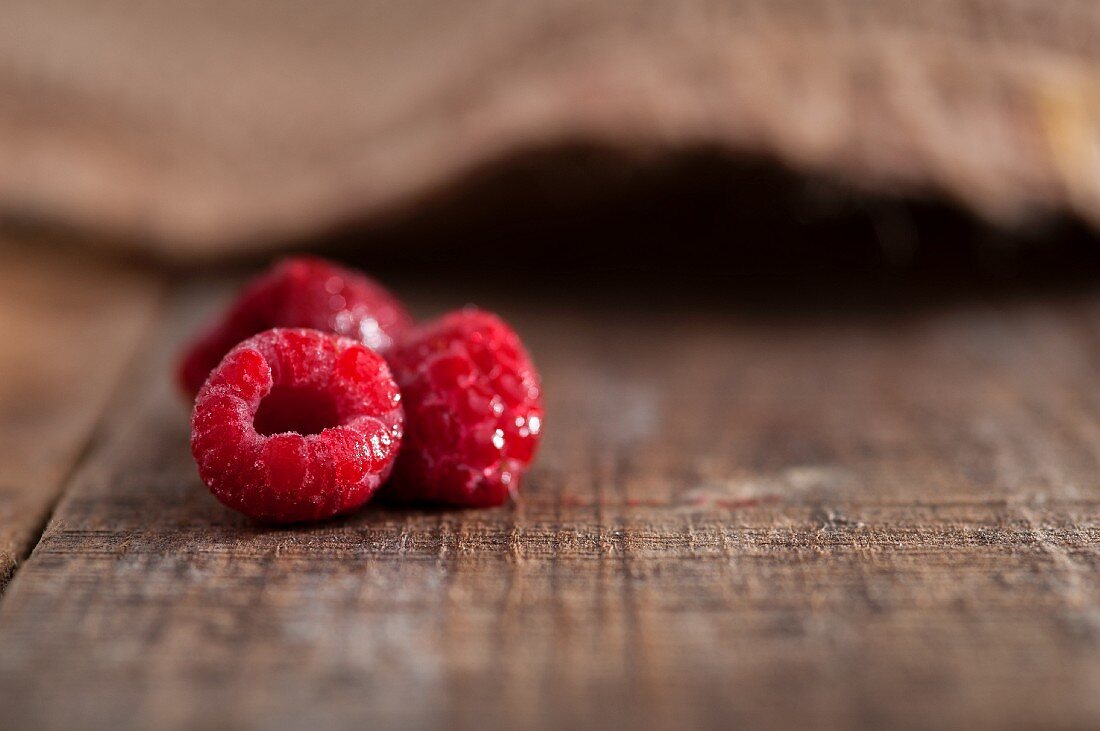 Three frozen raspberries on a rustic surface