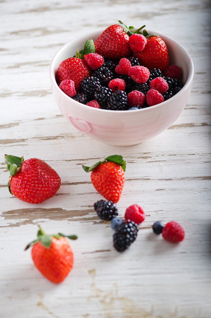 Verschiedene Beeren in Schüssel und auf Holzuntergrund