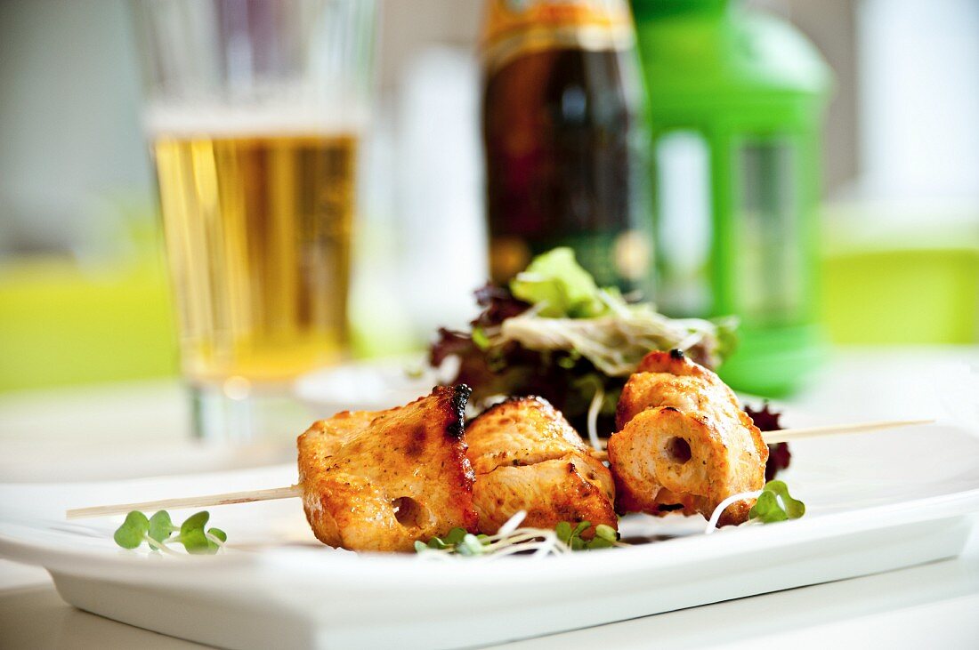 A chicken skewer with salad, served with a glass of beer