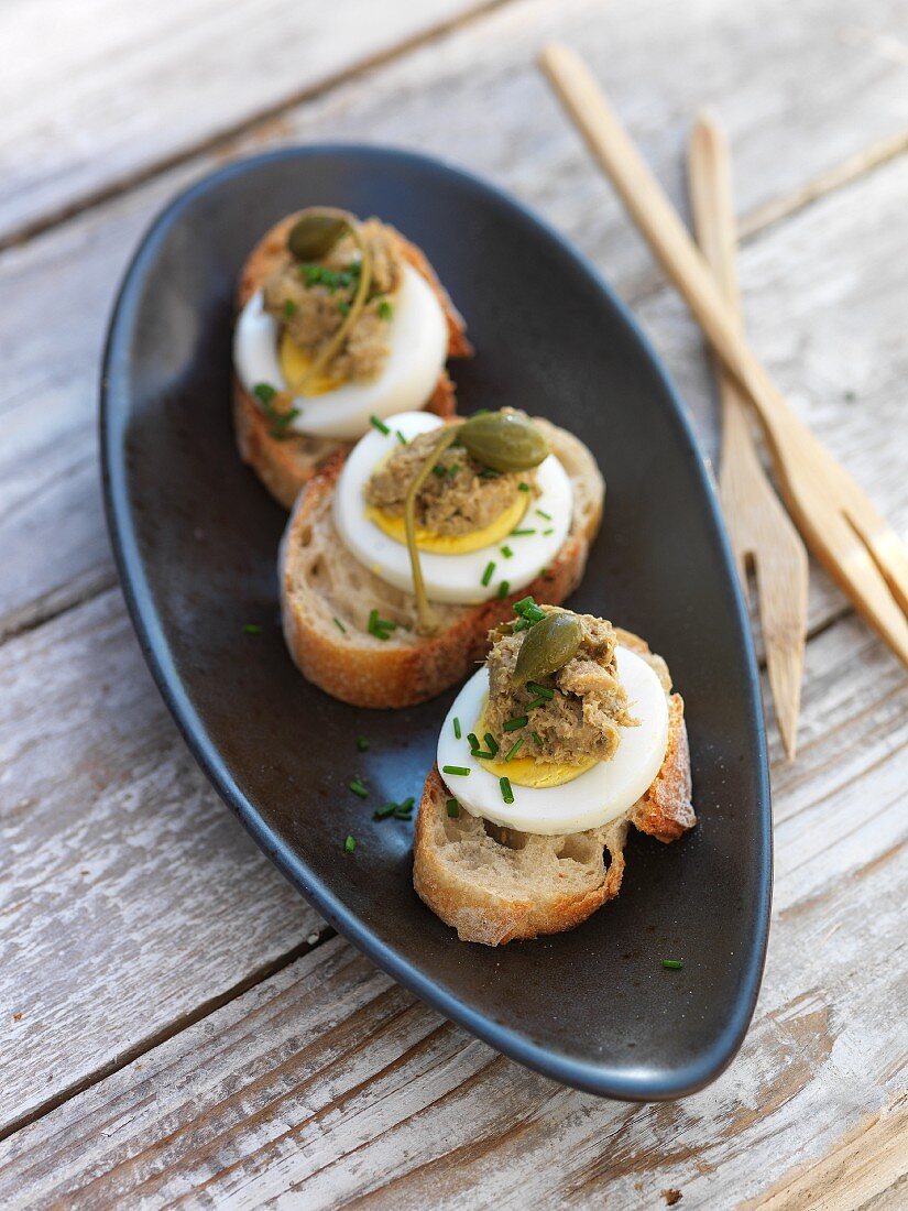 Mini open sandwiches topped with egg, anchovy paste and capers