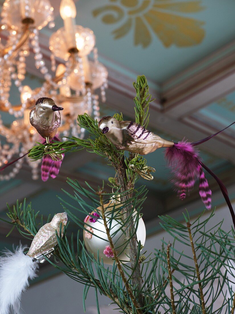 Silver bird figurines clipped to branches below lit chandelier