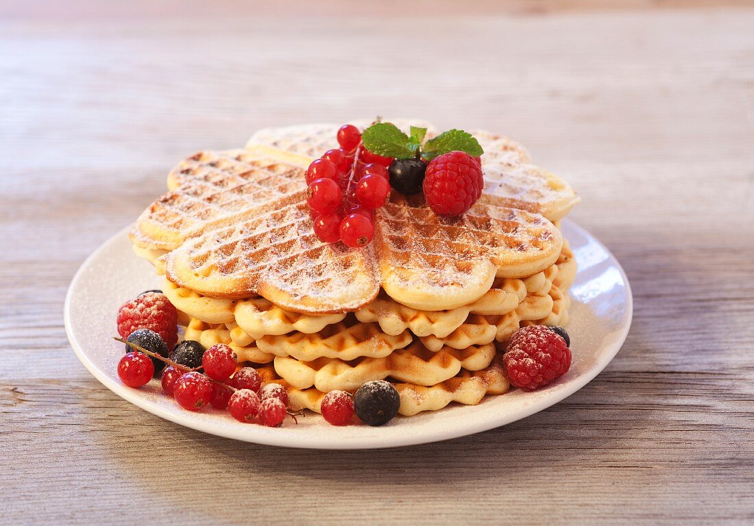 Waffles with raspberries, blueberries and redcurrants on a wooden plate