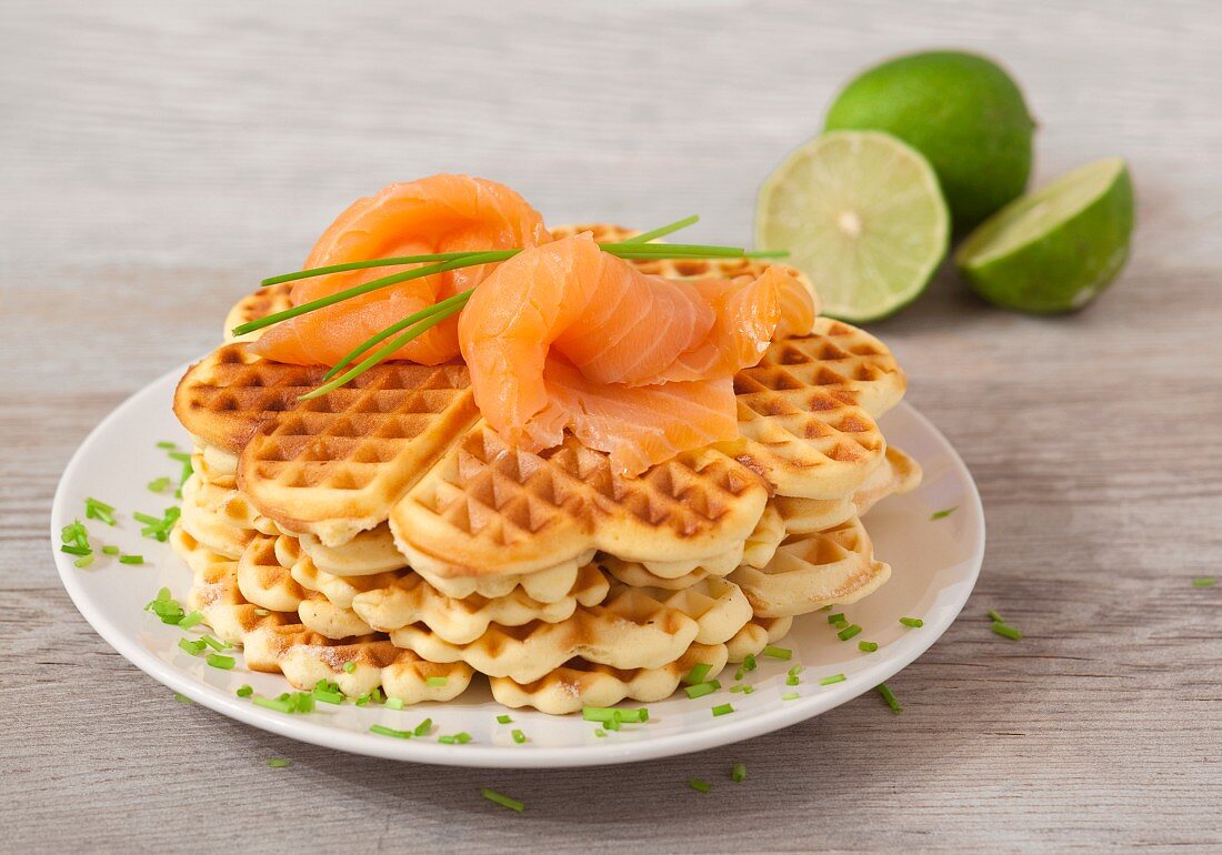 Waffles with salmon, limes and chives on a wooden surface