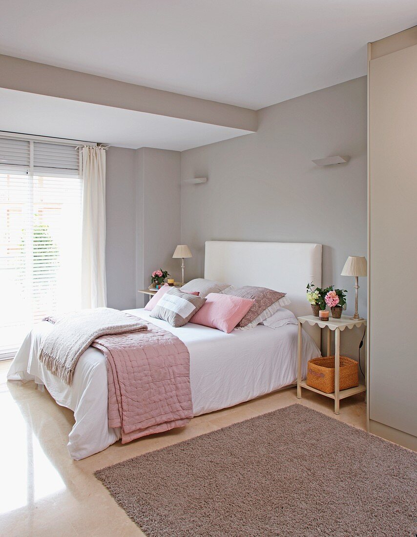 Doppelbett mit Decken und Zierkissen in zartem Grau und Rosa vor grau getönten Schlafzimmerwänden