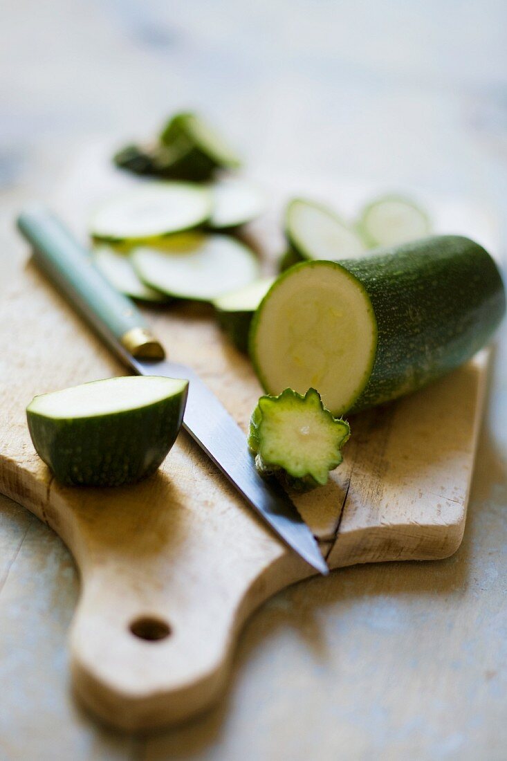 A courgette, partly sliced, on a chopping board