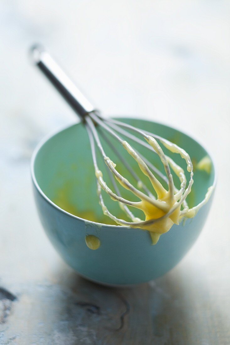 Egg whisk with remains of mayonnaise, laid across the top of the bowl