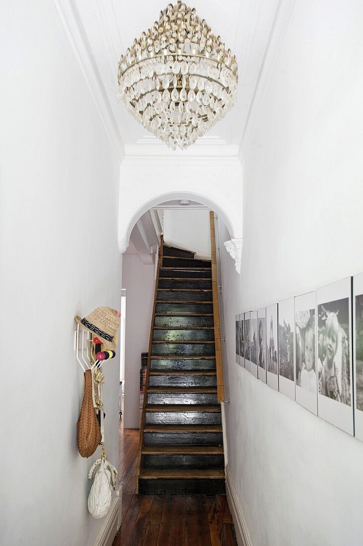 Chandelier on ceiling of narrow hallway with gallery of photos on wall in front of arched doorway and staircase in grand apartment