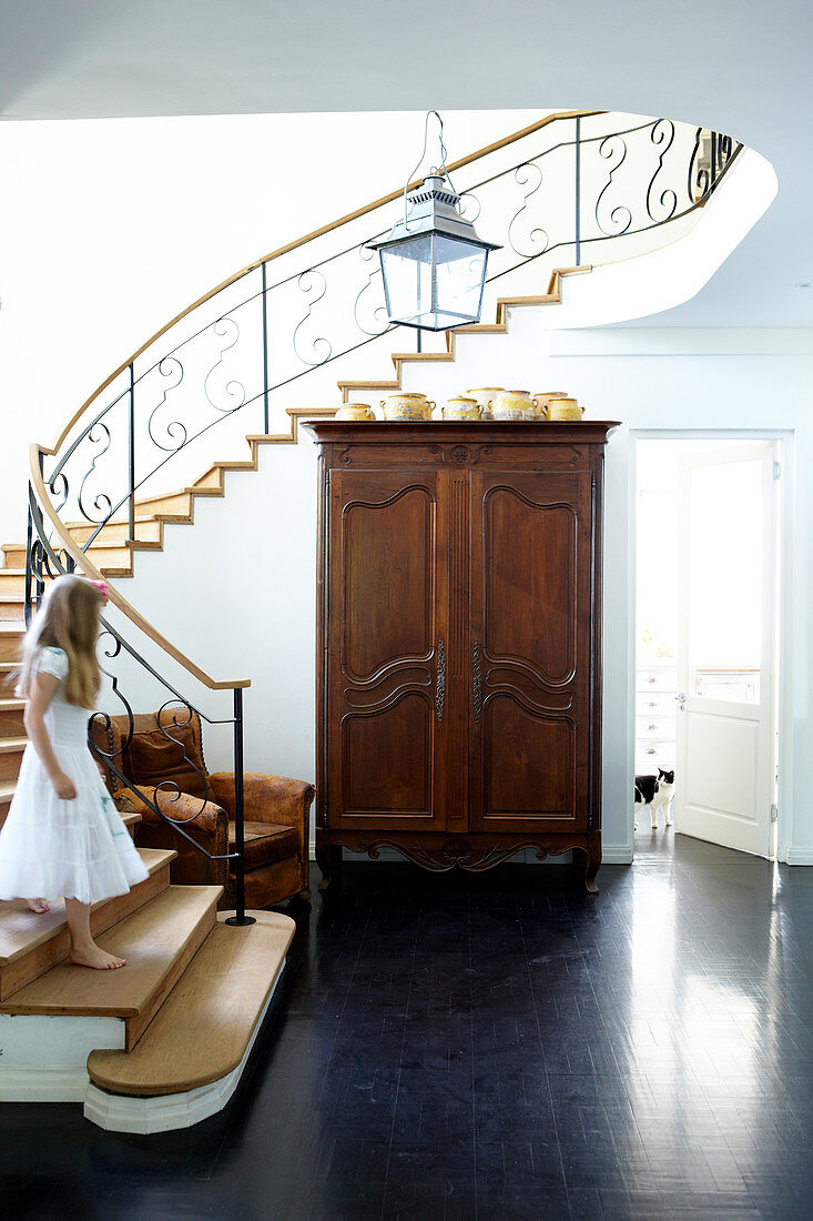 Spacious staircase with playful, wrought iron banister and antique wooden armoire in the lobby of a town home
