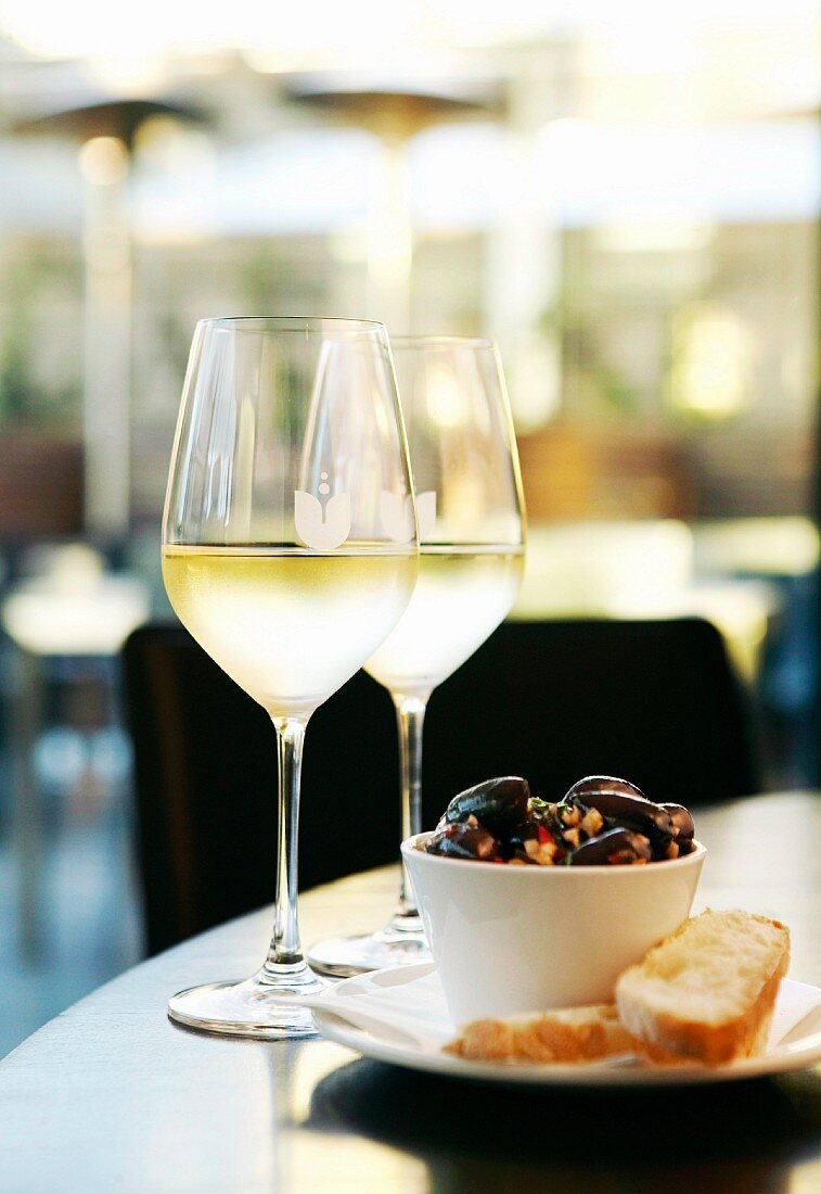 Sautéed olives with chorizo and white bread served with glasses of white wine