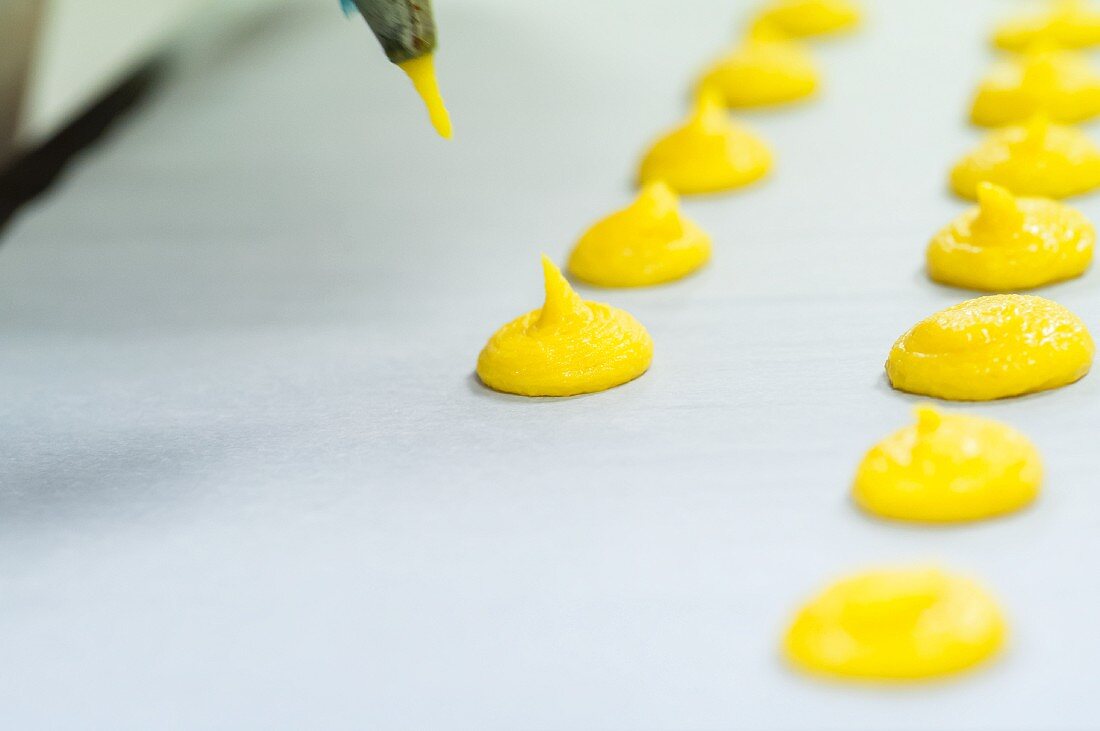 Mixture for yellow macaroons being piped onto grease-proof paper