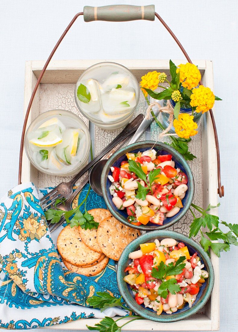 Two Bowls of Cherry Tomato and Bean Salad with Feta Cheese; Crackers and Drinks on a Tray