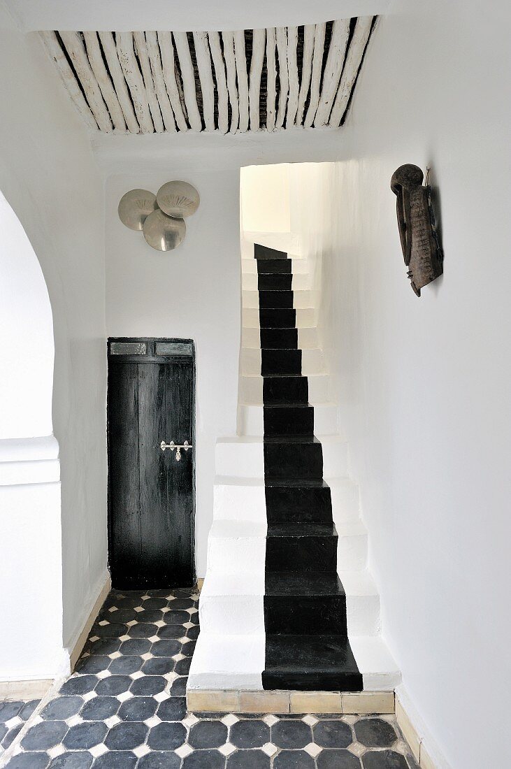 Fusion of Moroccan tradition and modern elements in foyer decorated in black and white with narrow staircase