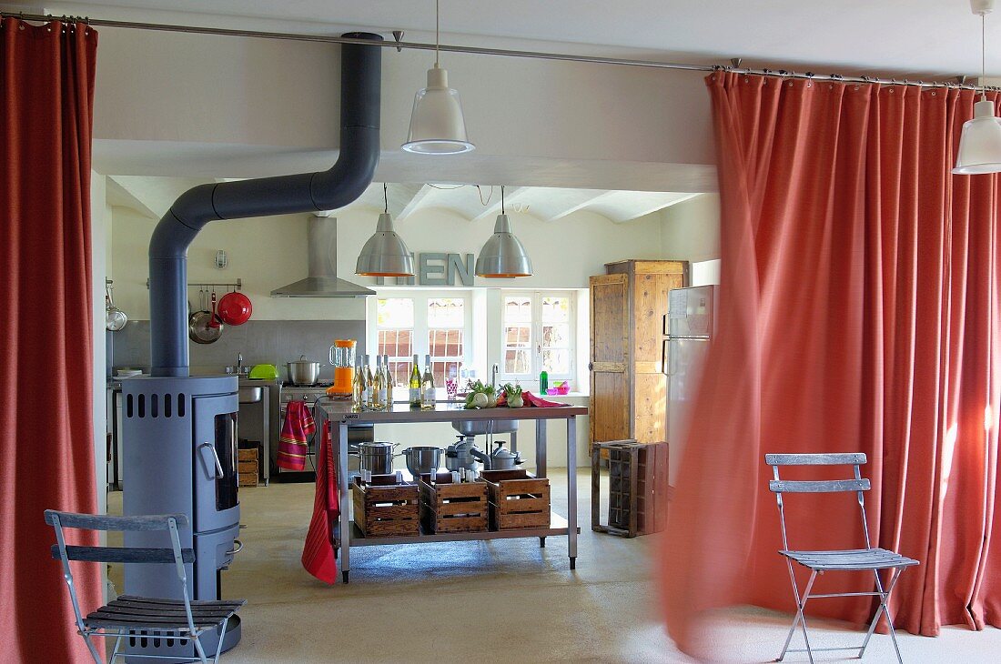 Converted farmhouse kitchen with sink unit and free-standing log burner separated from living room by wafting curtain