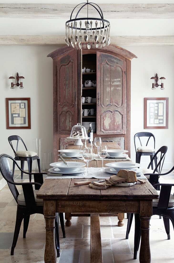 Place settings on antique table and retro-style chairs in front of farmhouse cupboard in elegant, rustic dining room