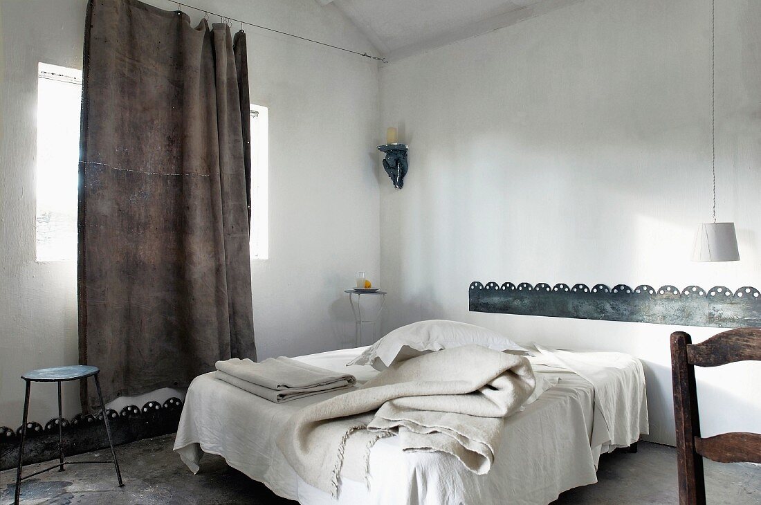 Various blankets on French bed, casual linen curtain hung from taut wire and sheet metal bands as borders on wall