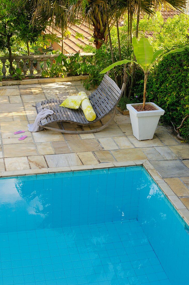 Wooden rocker lounger and potted palm on terrace next to pool
