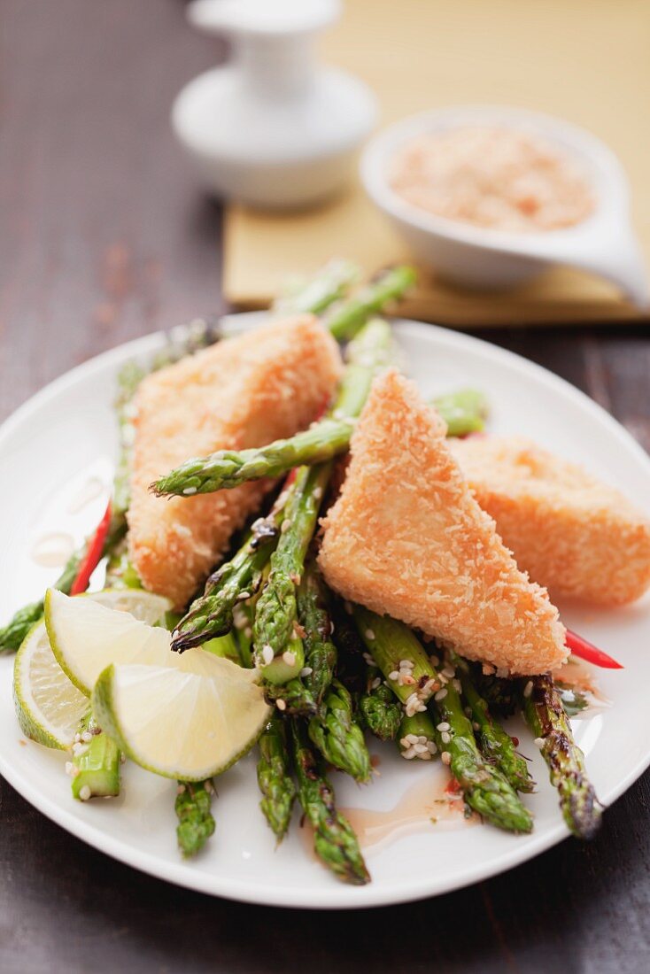 Breaded tofu on a bed of green asparagus with lime wedges