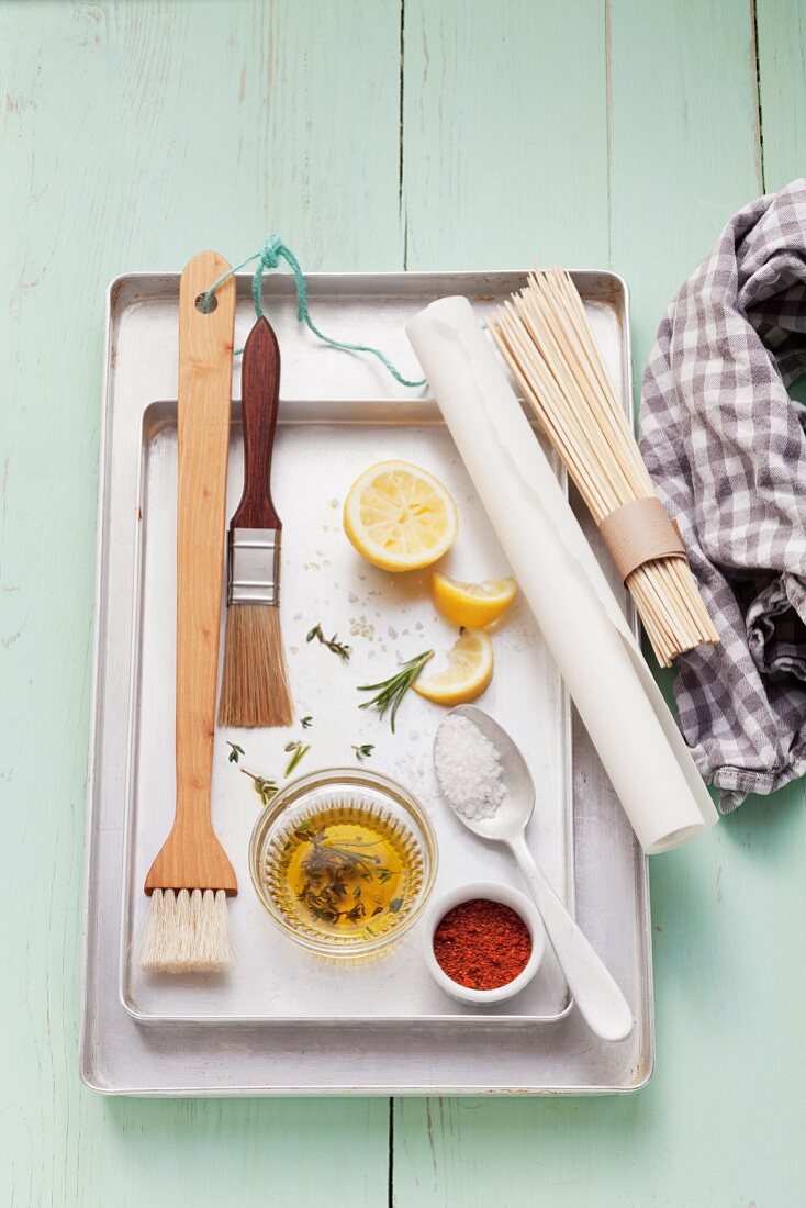 Assorted barbecue utensils, seasonings, lemons and olive oil on a grill pan